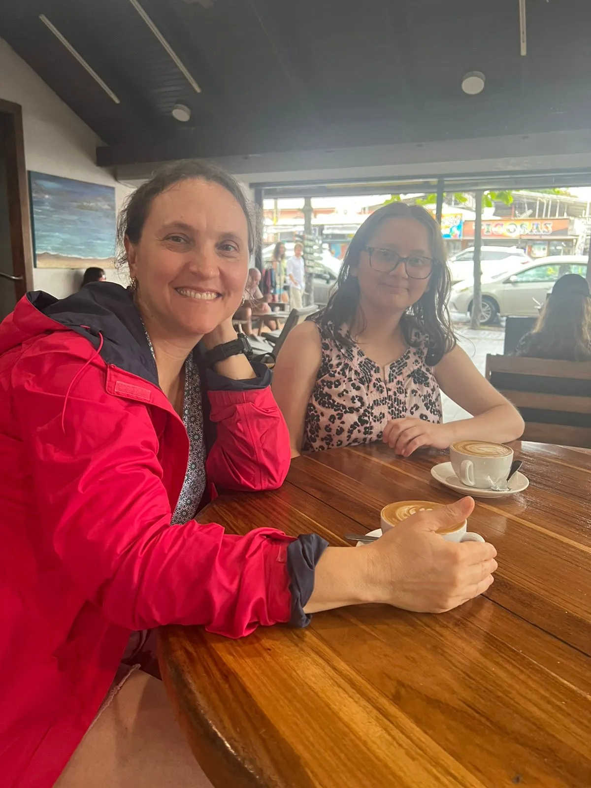 Two people enjoying lattes at an open-air cafe in Jaco, Costa Rica with a street view background