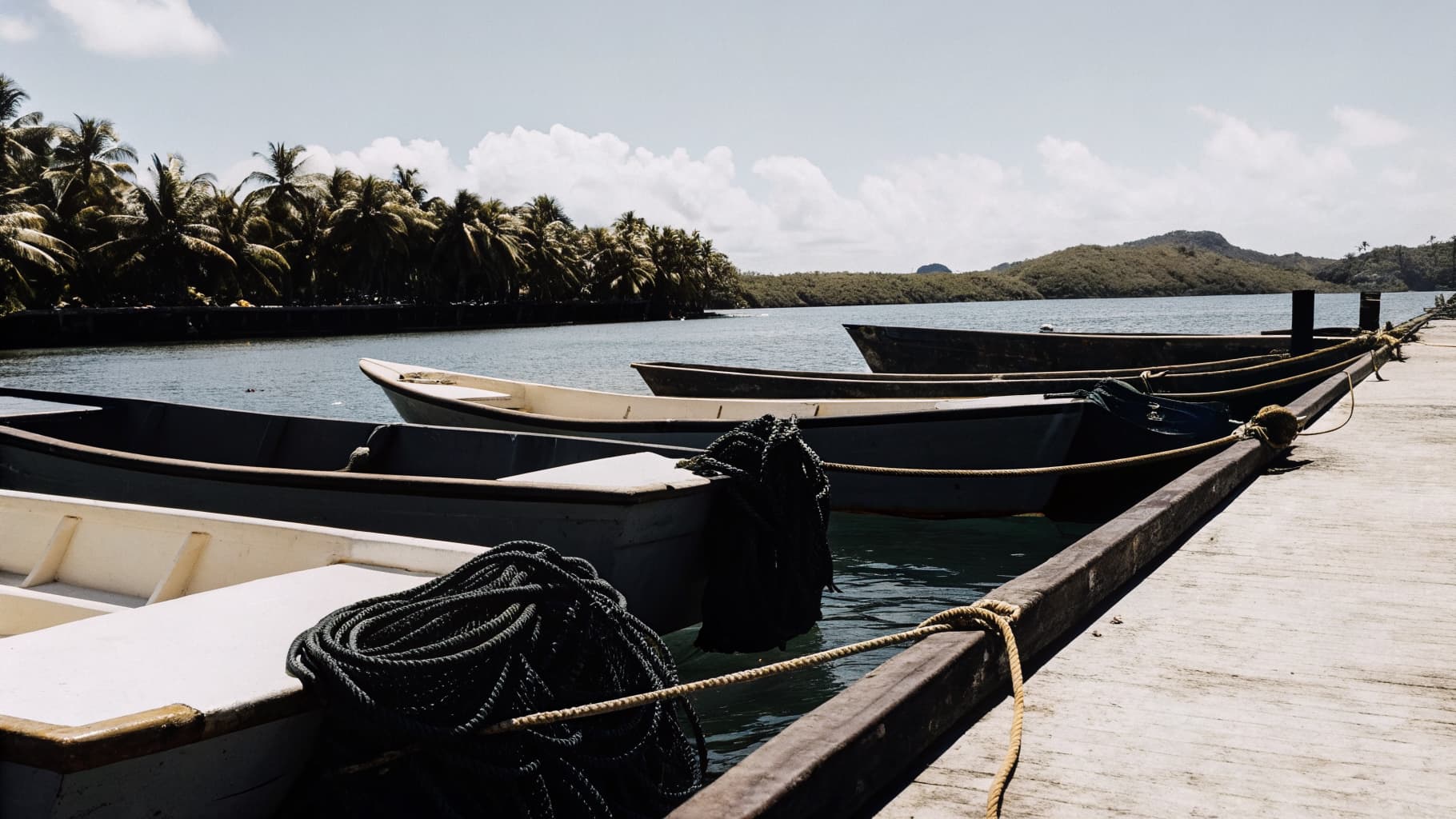 Wooden fishing pangas moored at a quiet marina in Jaco Costa Rica with palm trees and green jungle hills in the background