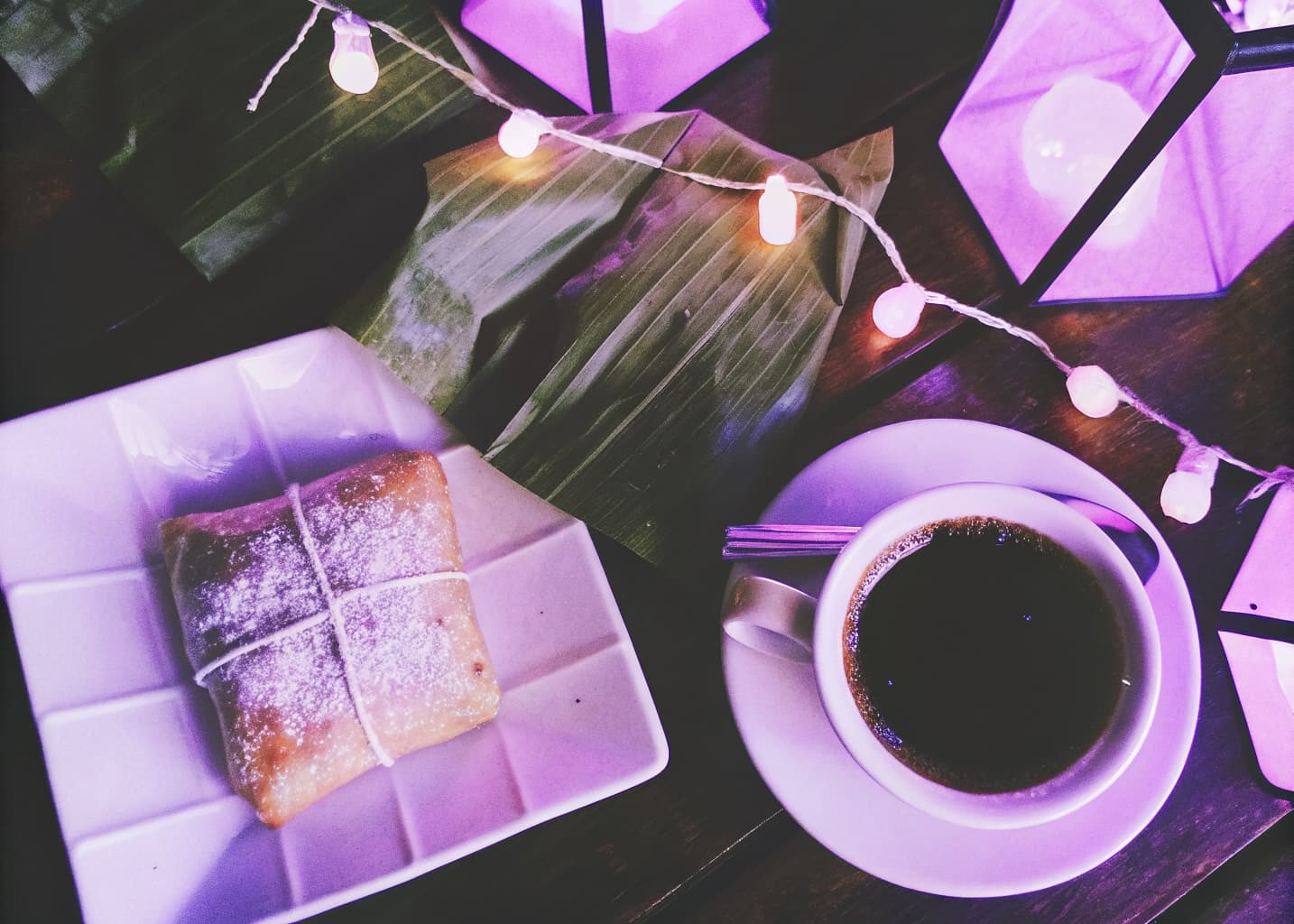 Traditional Costa Rican Independence Day food spread with banana-leaf tamales, torta chilena pastry, and coffee on a wooden table with string lights