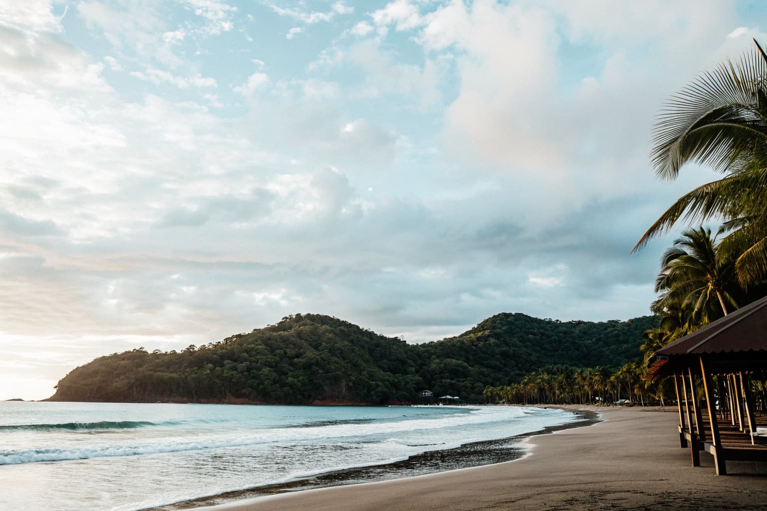Jaco Beach Costa Rica in September — misty green jungle hills, palm trees, and a golden sand shoreline along the Pacific coast