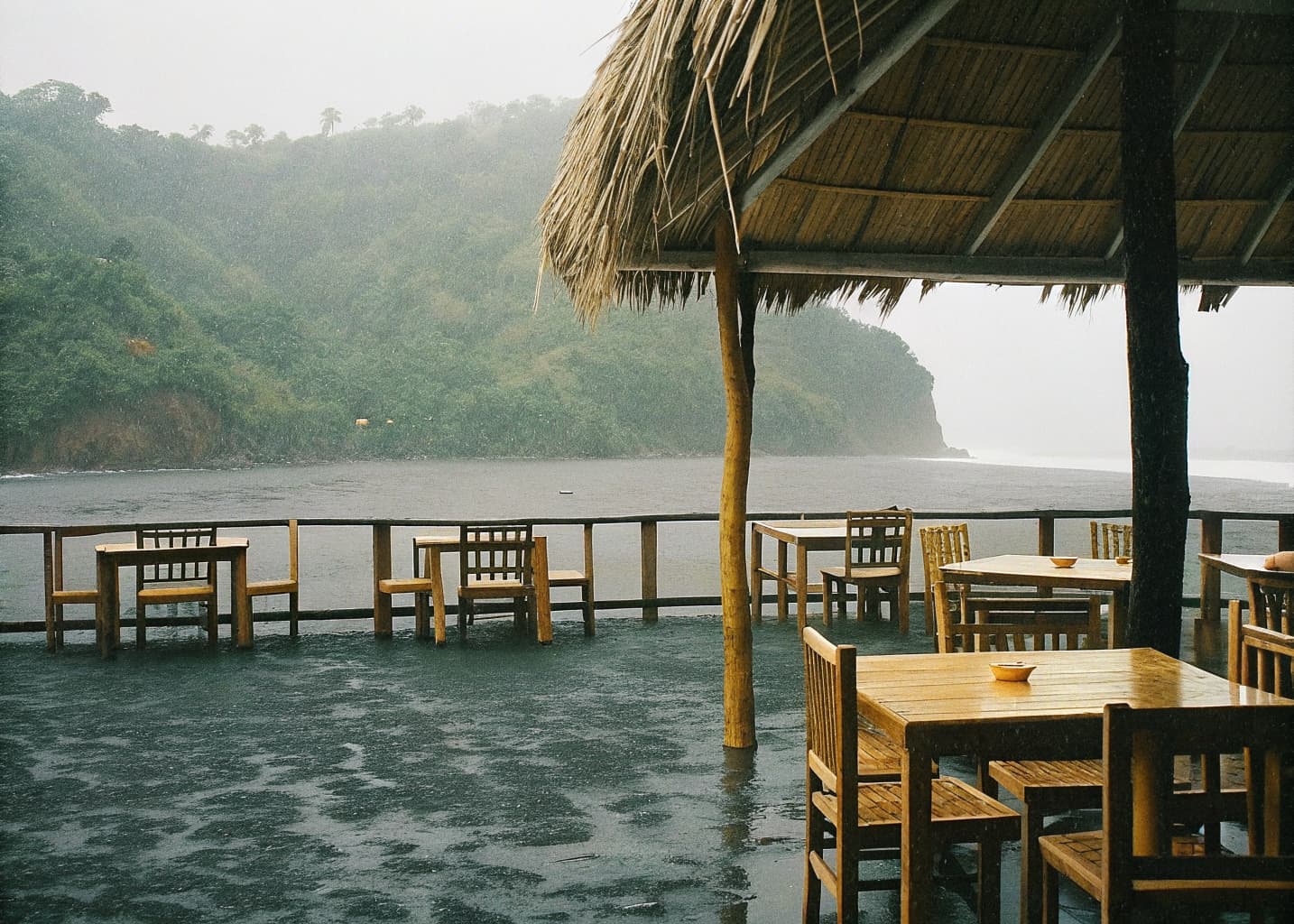 Empty open-air palapa restaurant in Jaco Costa Rica overlooking the misty green hills and grey Pacific ocean during a September rain shower